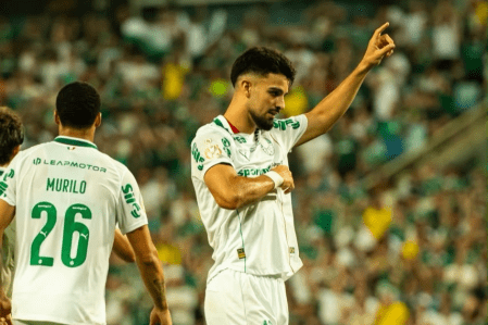 Flaco López e Murilo comemoram gol da classificação do Palmeiras na Copa do Brasil Atacante Flaco López comemora gol do Palmeiras apontando para cima, vestindo o uniforme branco. Em primeiro plano, o zagueiro Murilo aparece de costas com a camisa número 26. Ao fundo, torcida na arquibancada.